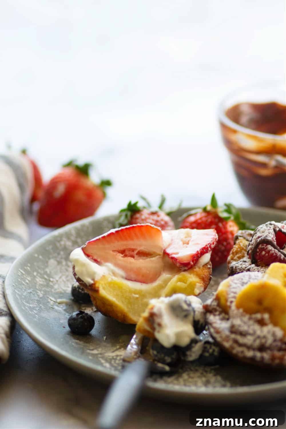Mini Dutch Baby Bites 5 Close-up of a Mini Dutch Baby Pancake generously topped with fresh raspberries and a decadent drizzle of melted chocolate, highlighting its puffed edges and delicious filling.