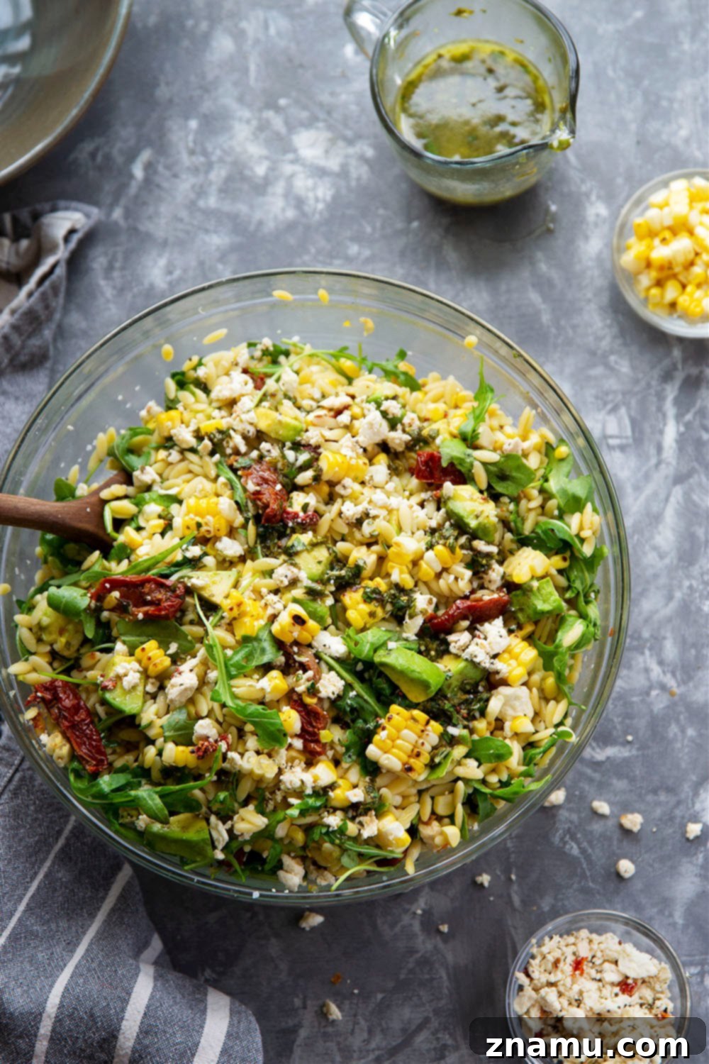 Smoky Corn & Sun-Kissed Tomato Orzo Salad 2 Overhead view of a colorful sun-dried tomato orzo salad in a mixing bowl, featuring charred corn, avocado, and feta.