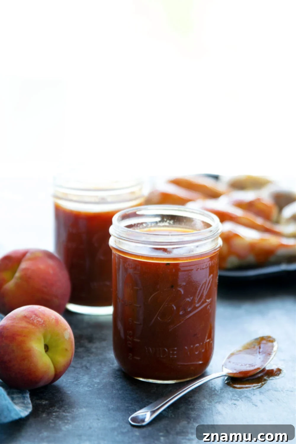 Sweet Heat Peach Chipotle Glaze 5 A wooden spoon stirring homemade Chipotle Peach BBQ Sauce in a saucepan as it simmers, showing its rich color.