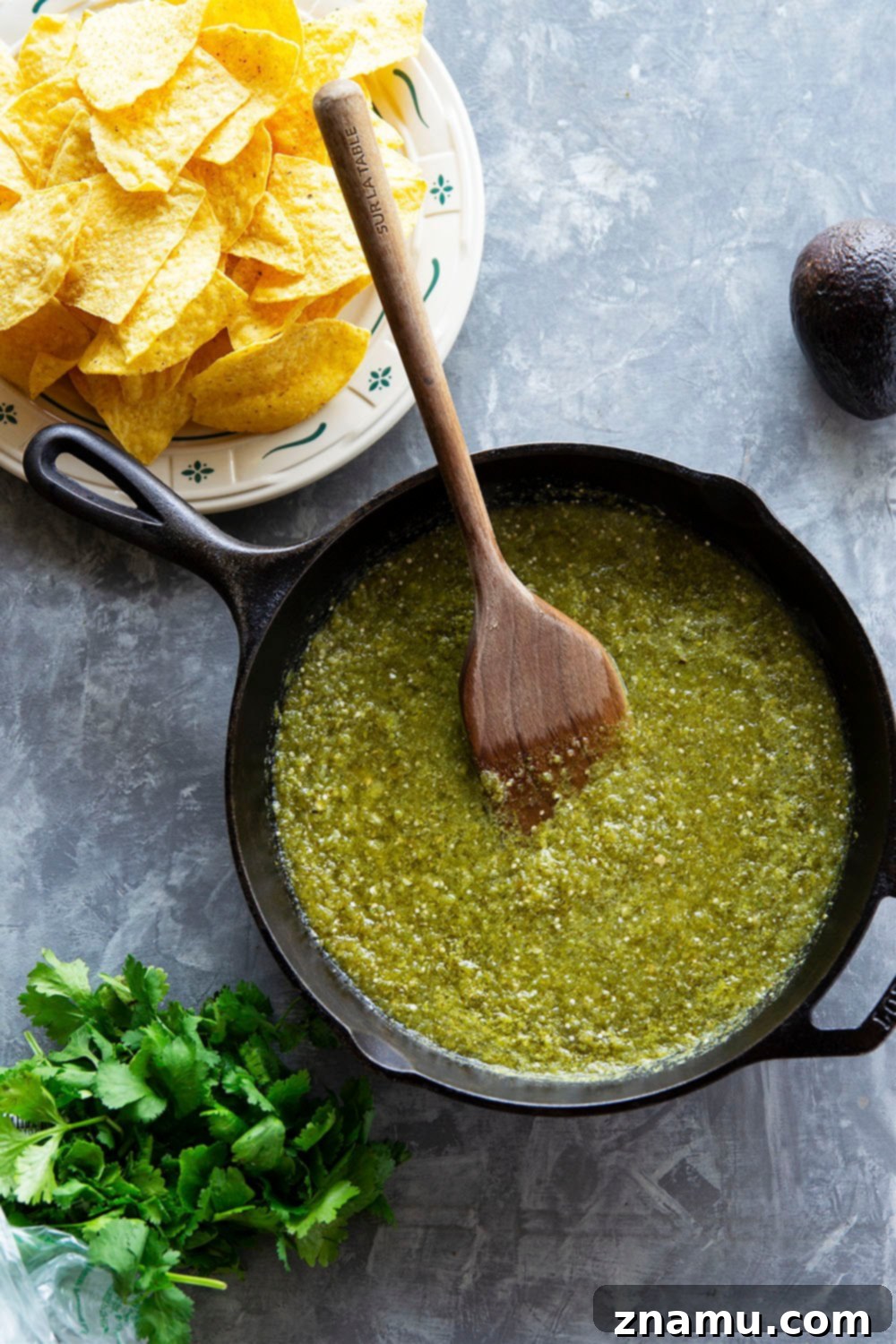 A close-up of a skillet of Chilaquiles Verdes, showcasing the vibrant green salsa, crispy chips, and toppings like fried egg and charred corn.