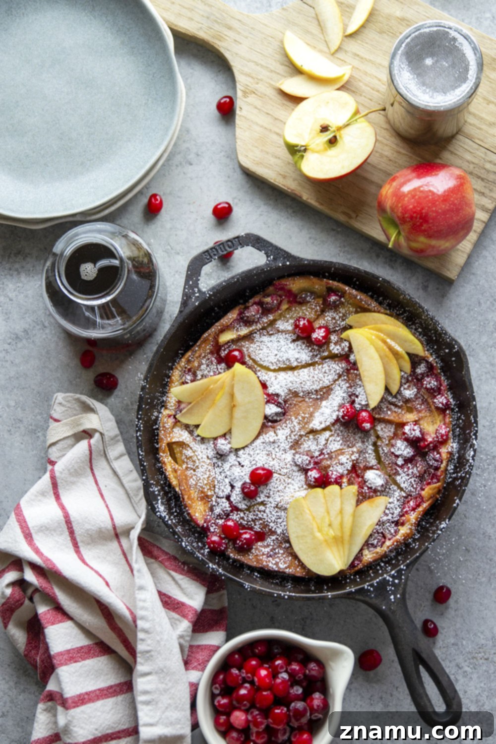Puffed Cranberry Apple Dutch Baby 4 Slices of Cranberry Apple Dutch Baby served on a plate, garnished with powdered sugar and maple syrup, highlighting the delicious fall fruit filling.