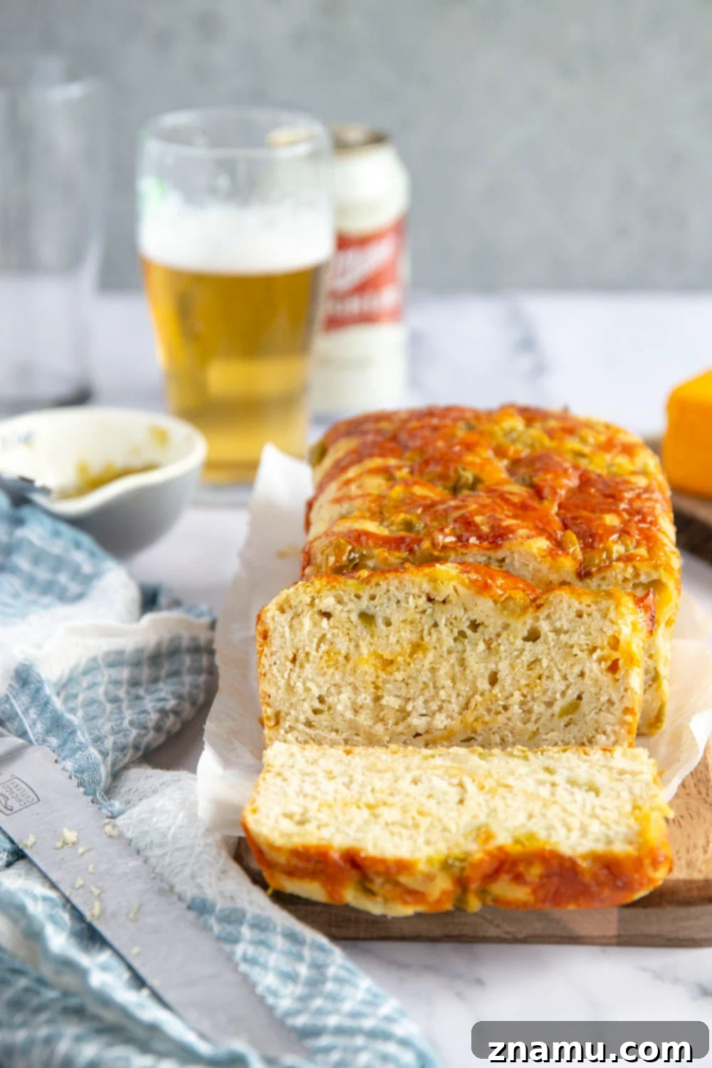Green Chile Cheddar Ale Loaf 2 A golden-brown loaf of Green Chile Cheddar Beer Bread, featuring visible green chiles and melted cheddar cheese, served on a cutting board.