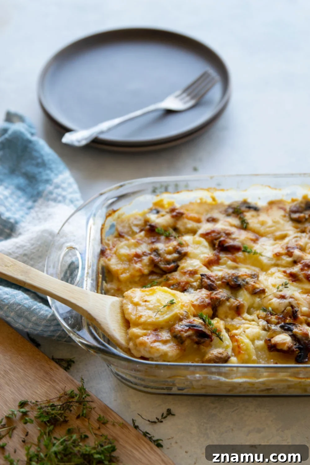A serving spoon lifting a generous portion of cheesy Caramelized Onion Scalloped Potatoes with Mushrooms from a baking dish.