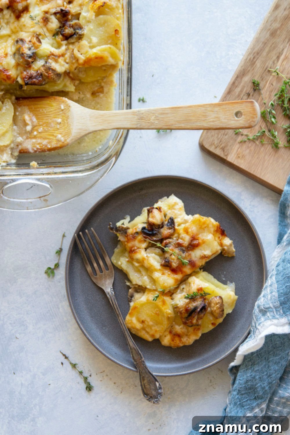 Full pan of golden-brown Caramelized Onion Scalloped Potatoes with Mushrooms, garnished with fresh thyme.