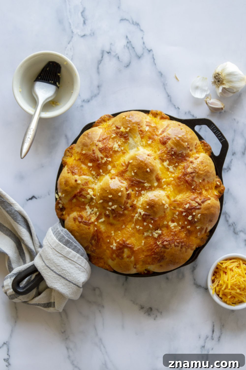 Skillet Garlic Cheddar Dinner Rolls 2 Golden-brown Garlic Cheddar Skillet Dinner Rolls in a cast iron pan, glistening with butter.