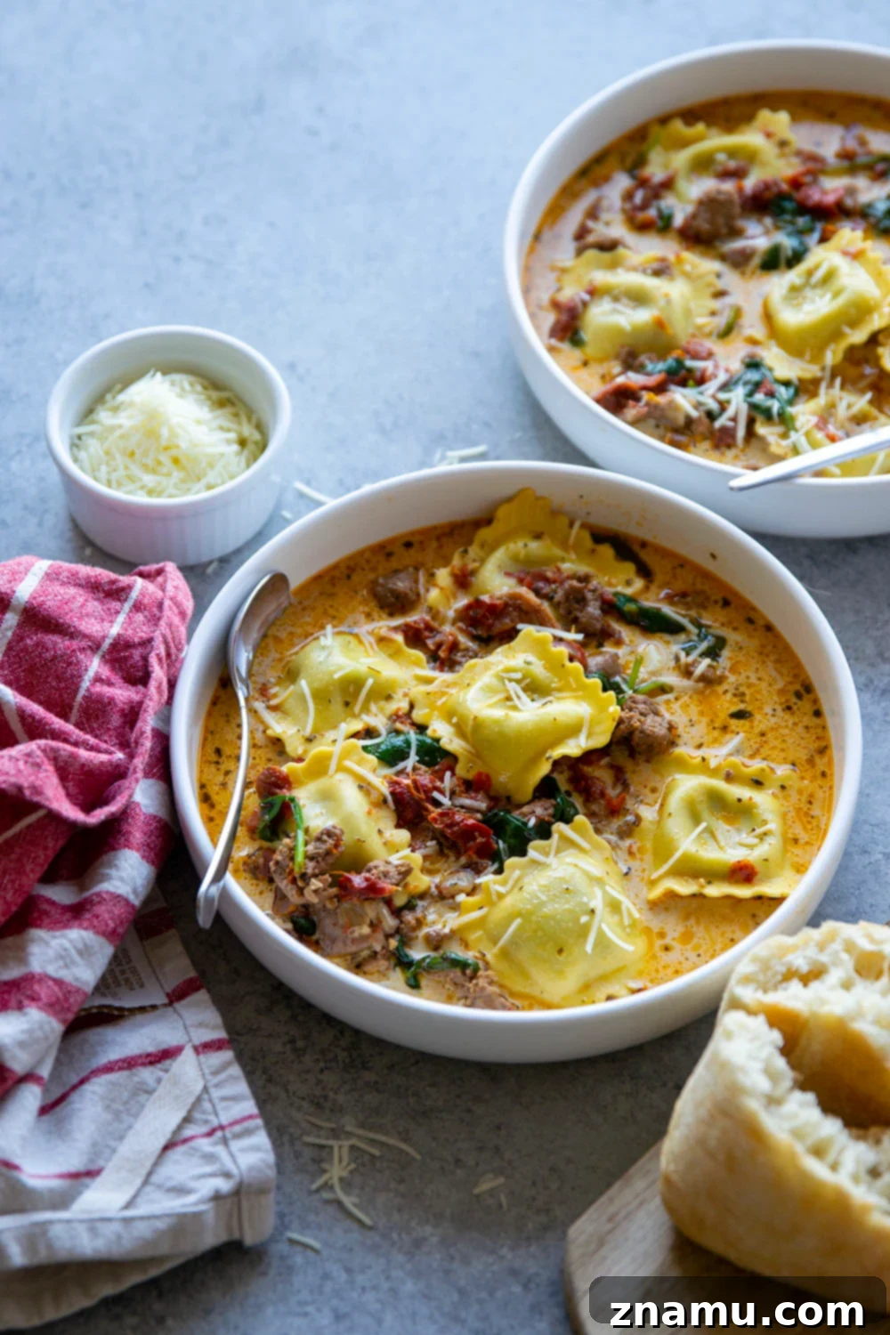A bowl of Tuscan Ravioli Soup on a rustic wooden table, with bread and a spoon, inviting to be eaten.