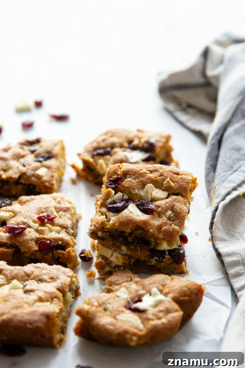 Blissful Cranberry White Chocolate Blondies 6 A stack of white chocolate cranberry blondies with one bite taken out, showing the gooey interior.