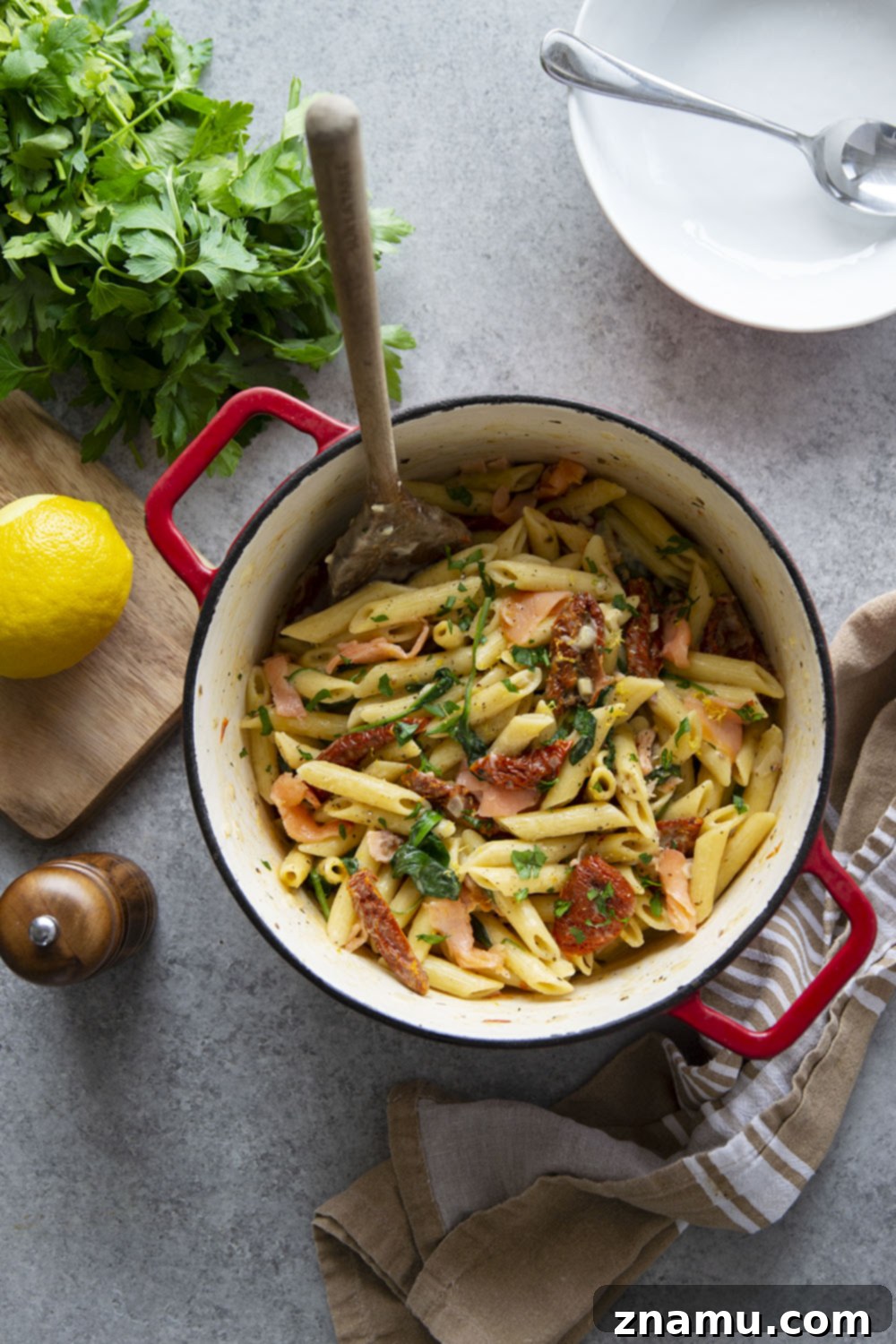Smoky Salmon Sun-Kissed Tomato Pasta 3 Overhead view of a large skillet filled with creamy sun-dried tomato smoked salmon pasta, garnished with fresh parsley, highlighting the rich texture and vibrant ingredients.