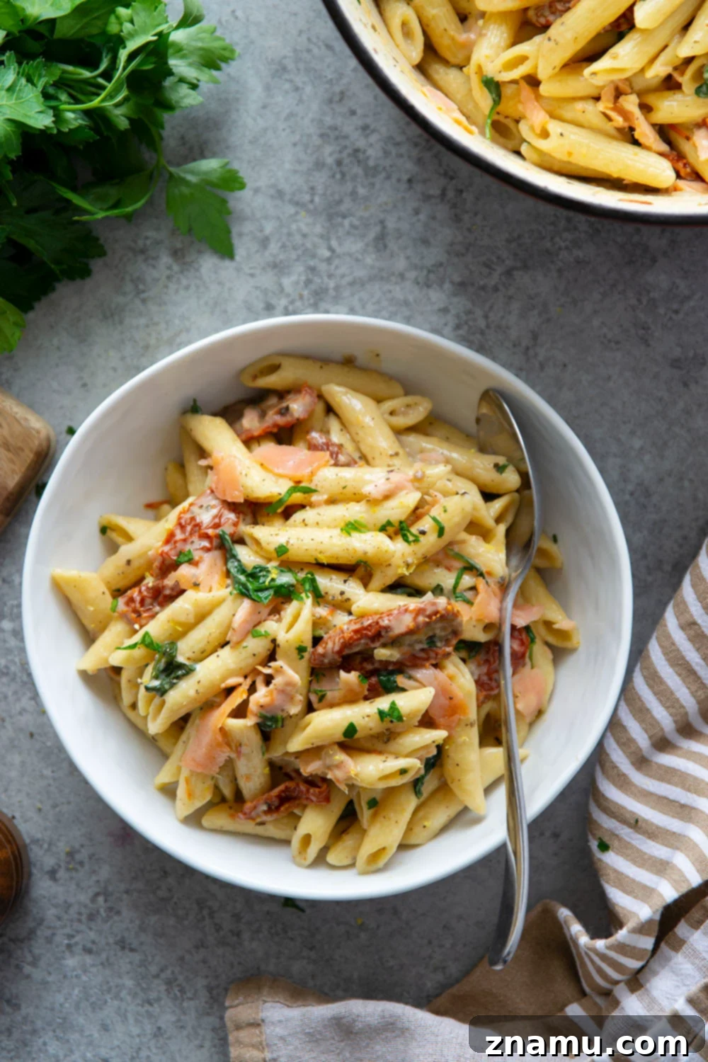 Smoky Salmon Sun-Kissed Tomato Pasta 4 Close-up of a serving of sun-dried tomato smoked salmon pasta, highlighting the creamy sauce clinging to the penne, with visible pieces of salmon and sun-dried tomatoes.