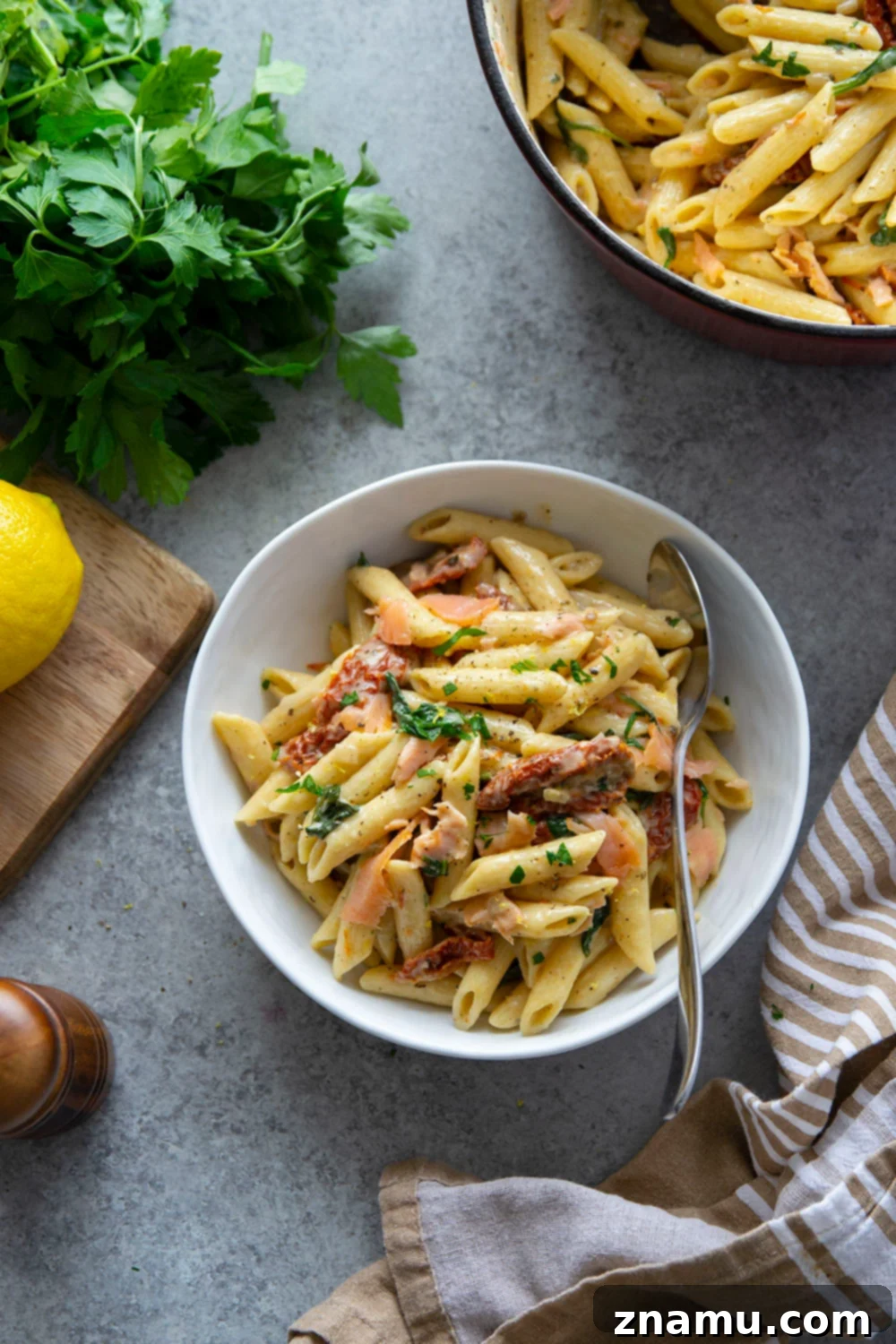 Smoky Salmon Sun-Kissed Tomato Pasta 6 A large serving bowl overflowing with creamy sun-dried tomato smoked salmon pasta, garnished generously with fresh parsley, ready to be enjoyed.