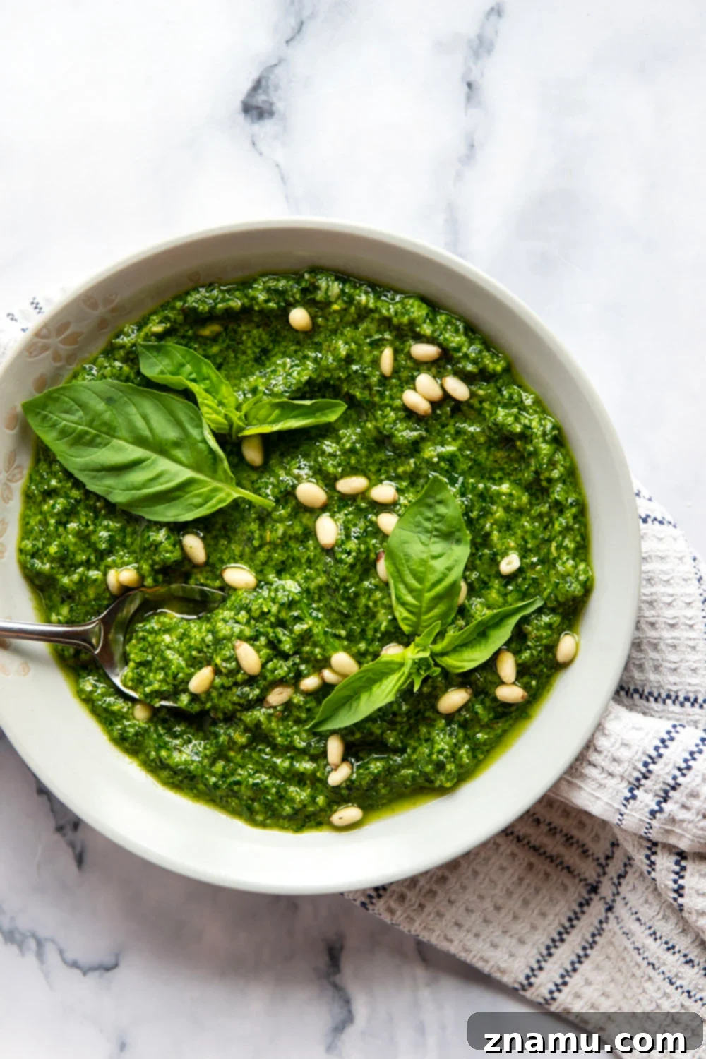 Emerald Spinach Basil Pesto 2 A close-up shot of vibrant green spinach basil pesto in a bowl, garnished with fresh basil leaves and pine nuts.