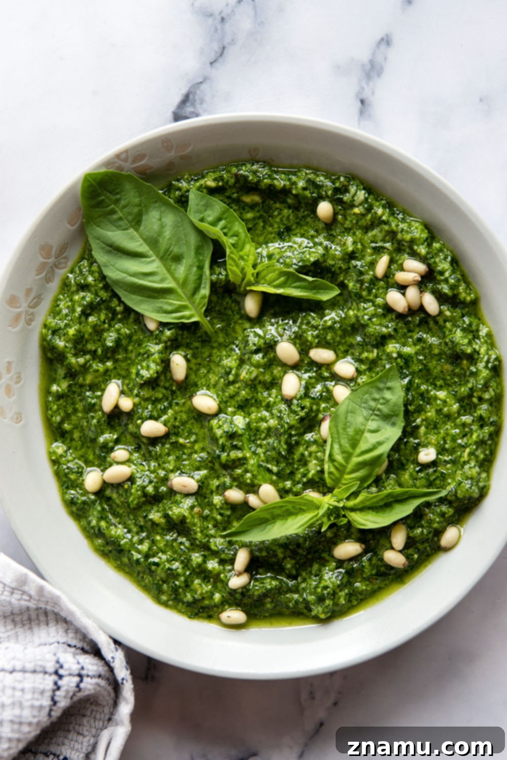 Emerald Spinach Basil Pesto 5 A glass jar filled with fresh spinach basil pesto, with a spoon resting inside, on a white background.
