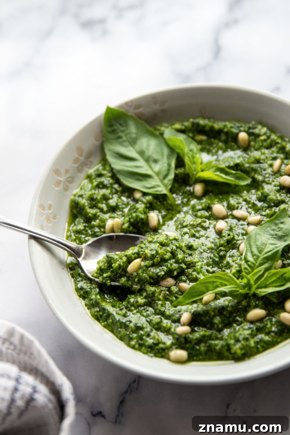 Emerald Spinach Basil Pesto 6 A bowl of freshly made spinach basil pesto accompanied by a small bunch of basil leaves and whole pine nuts.