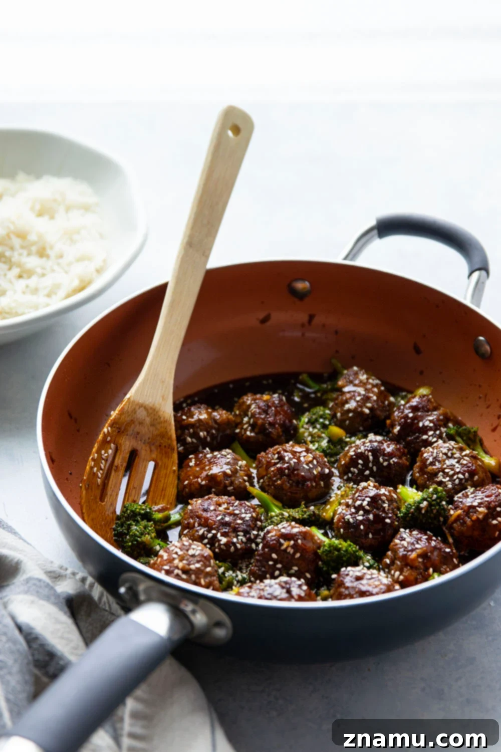 Sticky Sesame Beef & Broccoli Balls 3 A bowl of beef and broccoli meatballs served over fluffy white rice, garnished with sesame seeds.