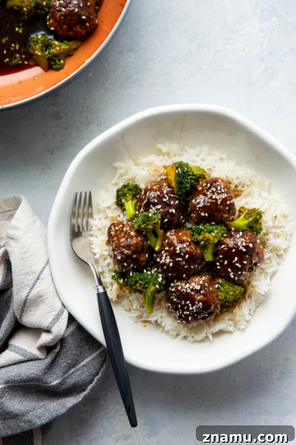Sticky Sesame Beef & Broccoli Balls 5 Close-up of beef and broccoli meatballs in a savory sauce in a skillet, garnished with sesame seeds.