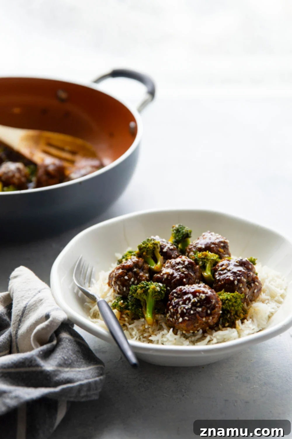 Sticky Sesame Beef & Broccoli Balls 6 Two hands holding chopsticks, picking up a juicy beef and broccoli meatball from a bowl.