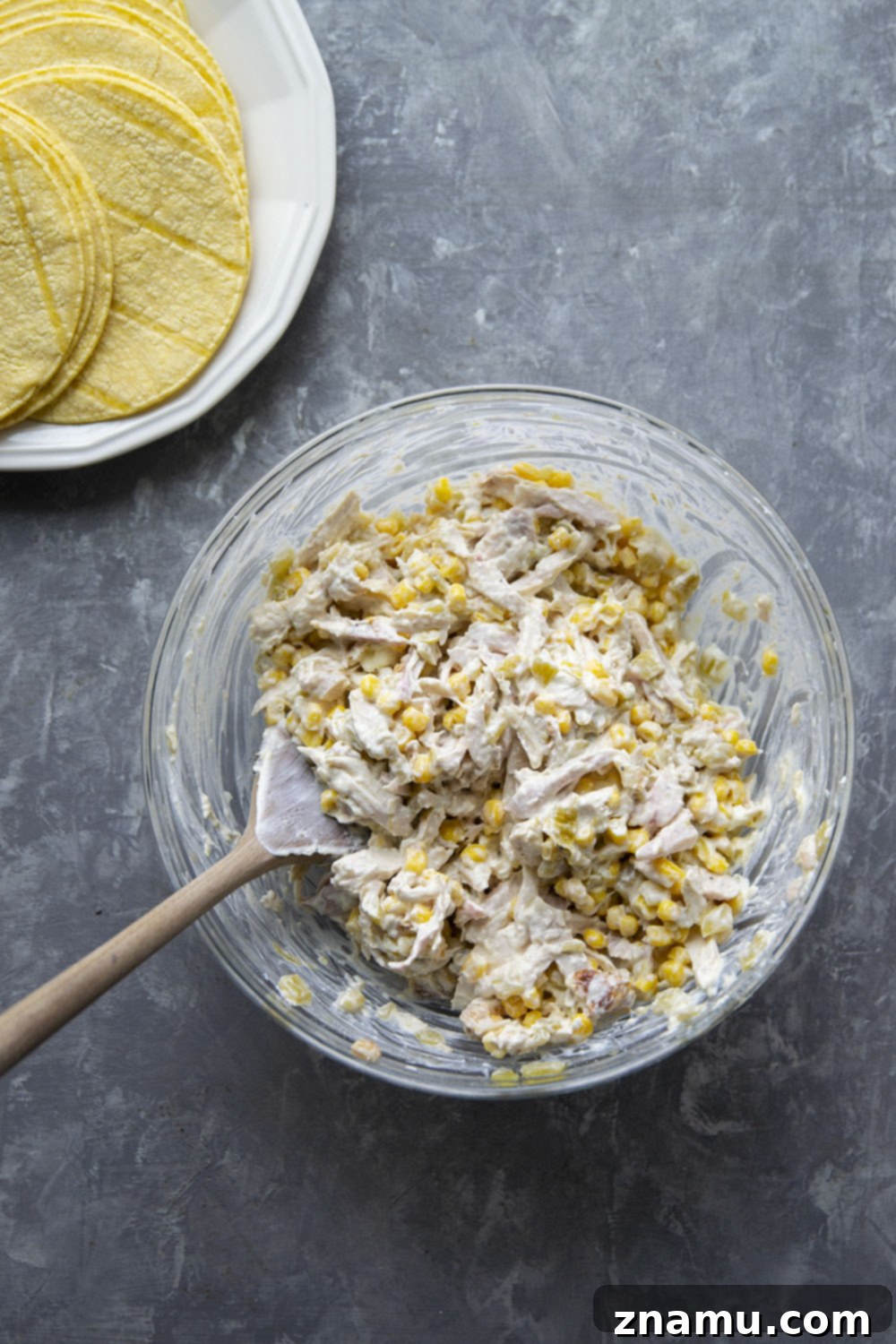 A vibrant, fully assembled skillet green chile chicken enchilada casserole, adorned with generous layers of melted cheese and ready to be baked to golden perfection.