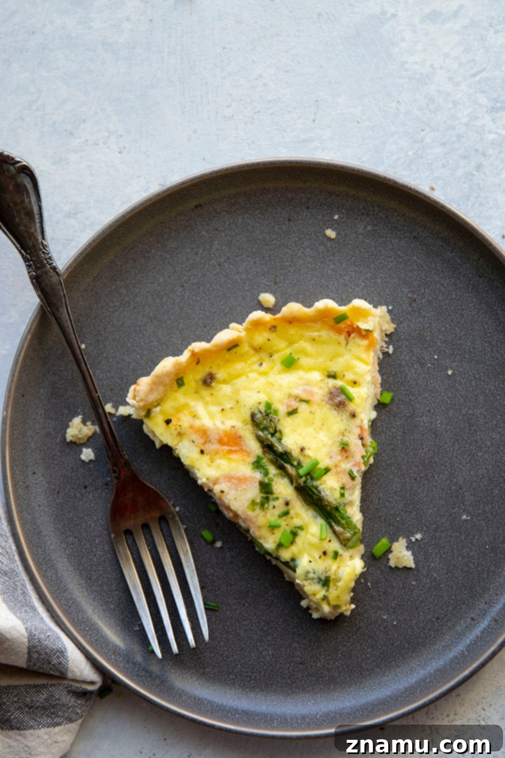 A beautifully golden Asparagus Smoked Salmon Quiche, ready to be sliced, on a wooden cutting board.