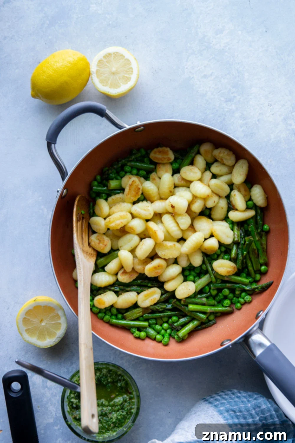 Close-up of fluffy gnocchi coated in green lemon pesto, mixed with bright green peas and tender asparagus tips.