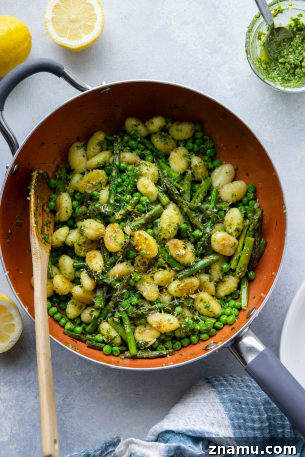 Overhead shot of a skillet filled with lemon pesto gnocchi, peas, and asparagus, garnished with fresh lemon zest and Parmesan.
