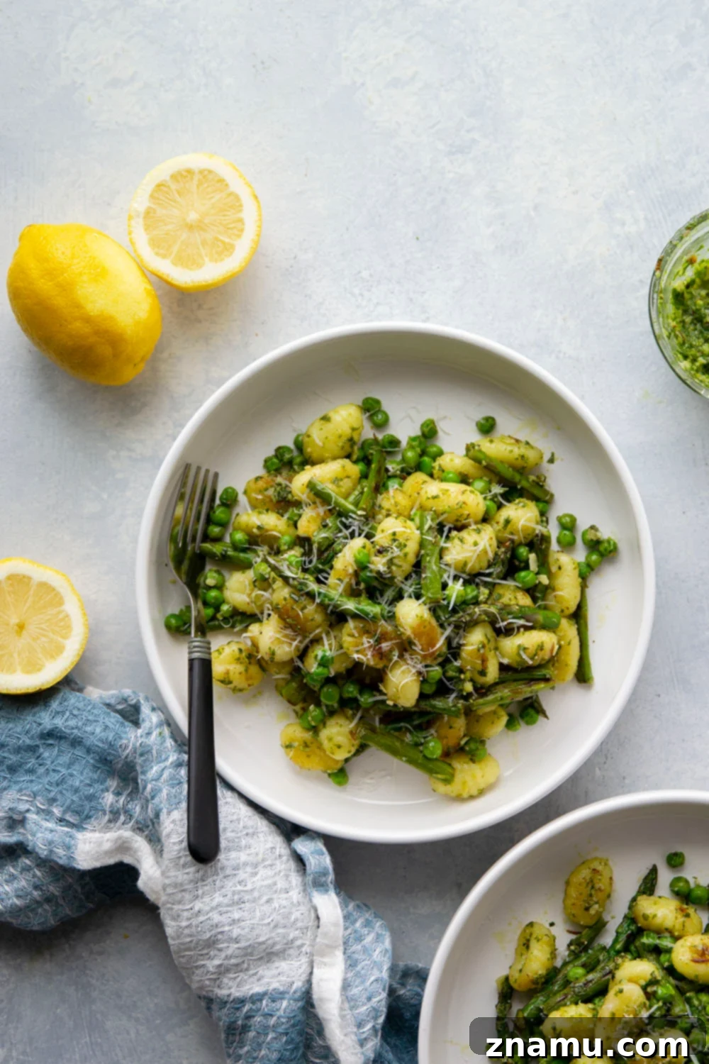 A serving of lemon pesto gnocchi with peas and asparagus in a white bowl, garnished with Parmesan.