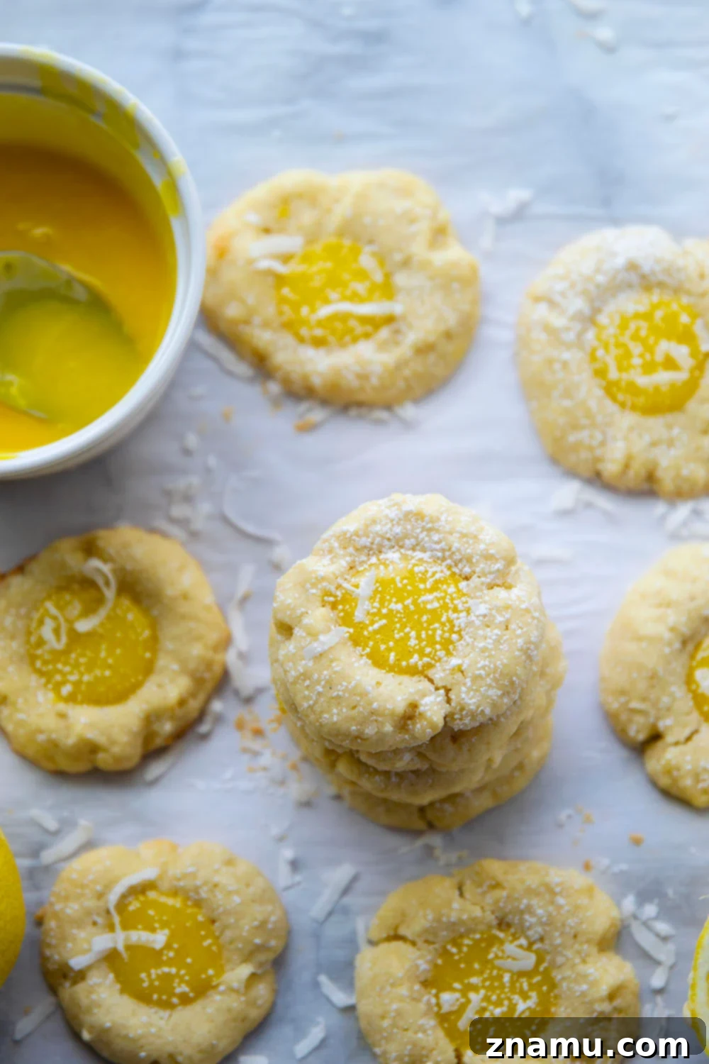 Coconut Lemon Curd Thumbprints 6 A stack of three lemon curd thumbprint cookies, showing off their golden crust and creamy lemon center, with a scattering of powdered sugar.