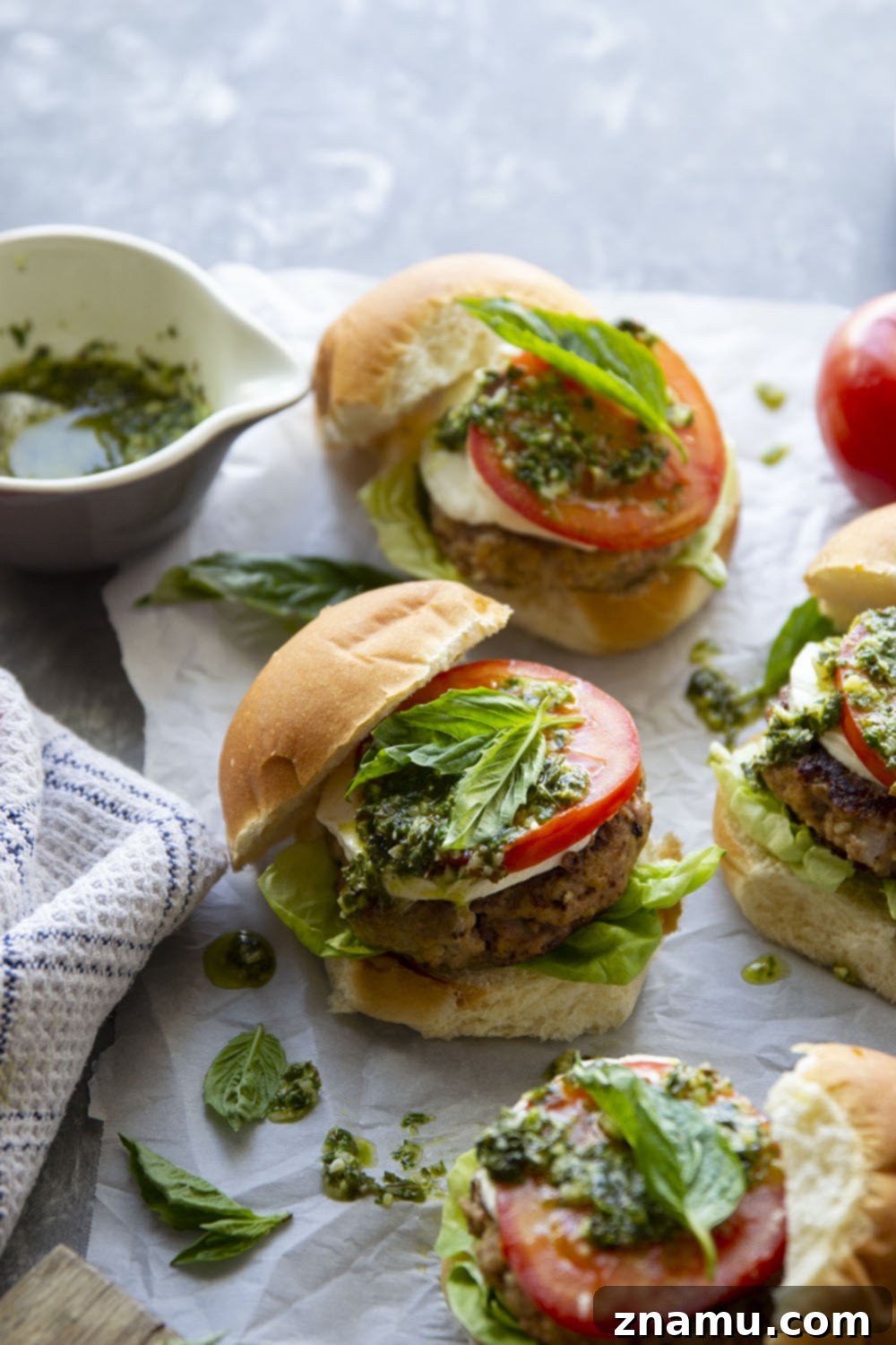 These Caprese Chicken Burgers are perfectly juicy and dressed up with all the caprese fixings and a flavorful pesto vinaigrette drizzled on top.