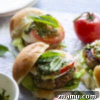 These Caprese Chicken Burgers are perfectly juicy and dressed up with all the caprese fixings and a flavorful pesto vinaigrette drizzled on top.