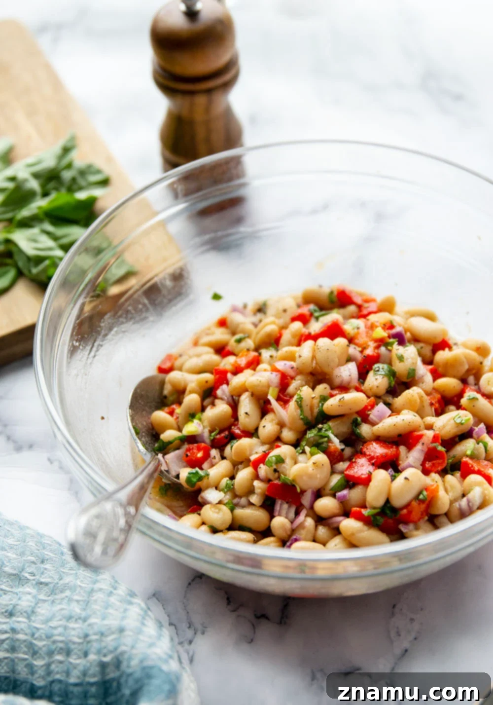 Miso Infused White Bean & Roasted Red Pepper Salad 6 Serving bowl filled with white bean salad, garnished with fresh basil leaves, ready to be shared at a gathering.