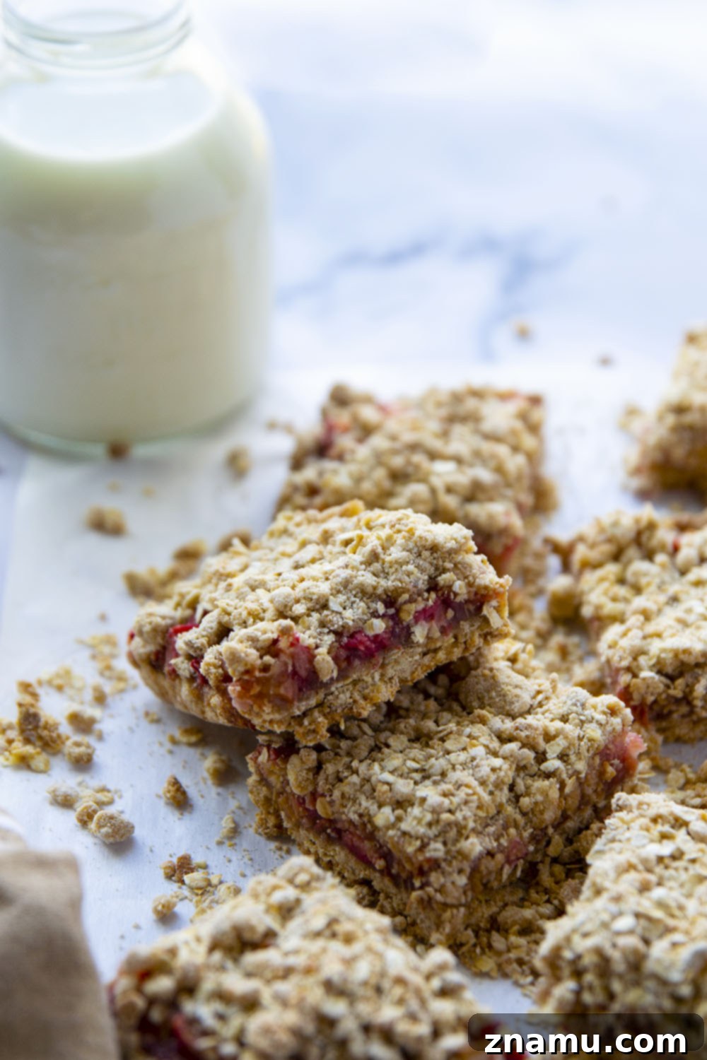 Summer Raspberry Rhubarb Crumble Bars 2 Freshly baked raspberry rhubarb oatmeal bars with a golden streusel topping, arranged on parchment paper.
