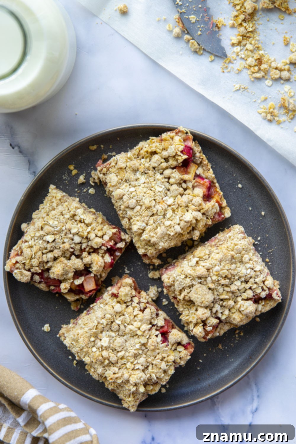 Summer Raspberry Rhubarb Crumble Bars 6 Several raspberry rhubarb oatmeal bars cooling on a wire rack, with some crumbs visible on the parchment paper.