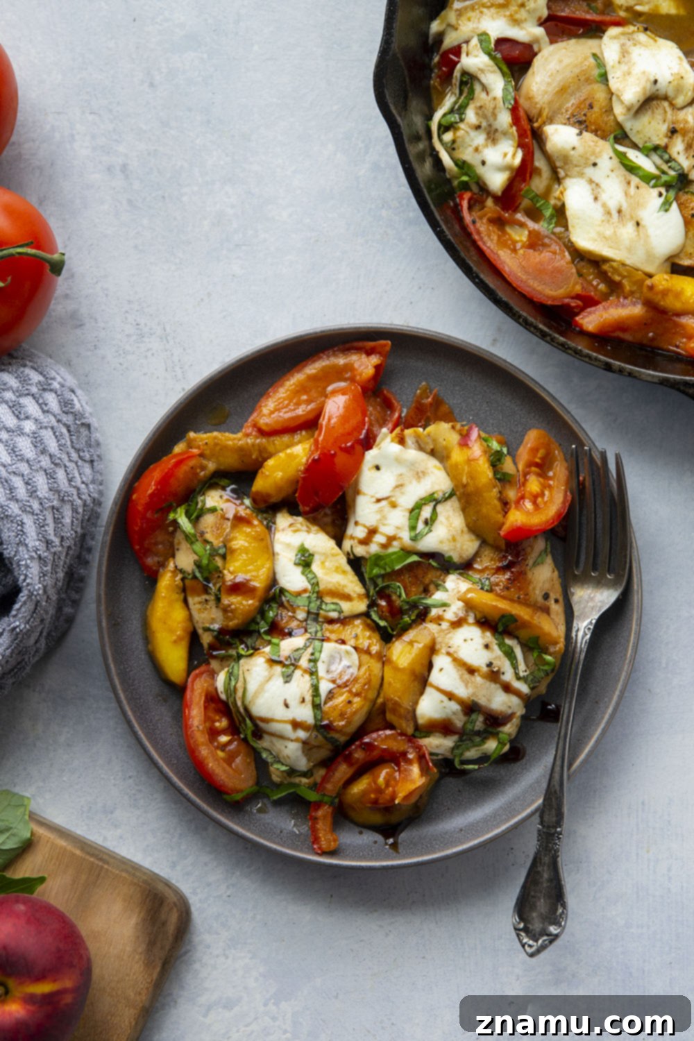 One-Pan Peach Caprese Chicken 3 Overhead shot of Caprese Peach Chicken in a cast iron skillet, showcasing seared chicken cutlets, peaches, tomatoes, mozzarella, and basil.