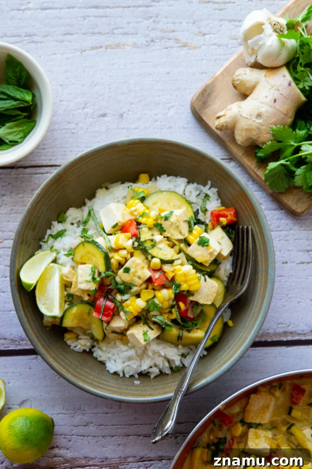 Vibrant Thai green curry tofu with sweet corn, zucchini, and bell peppers in a rich coconut sauce, served with rice.