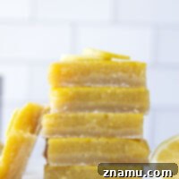 Individual lemon bar dusted with powdered sugar, sitting on a plate.