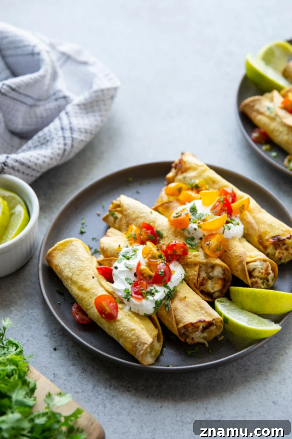 Platter of air fryer green chile chicken taquitos with various toppings like sour cream, salsa, and cilantro