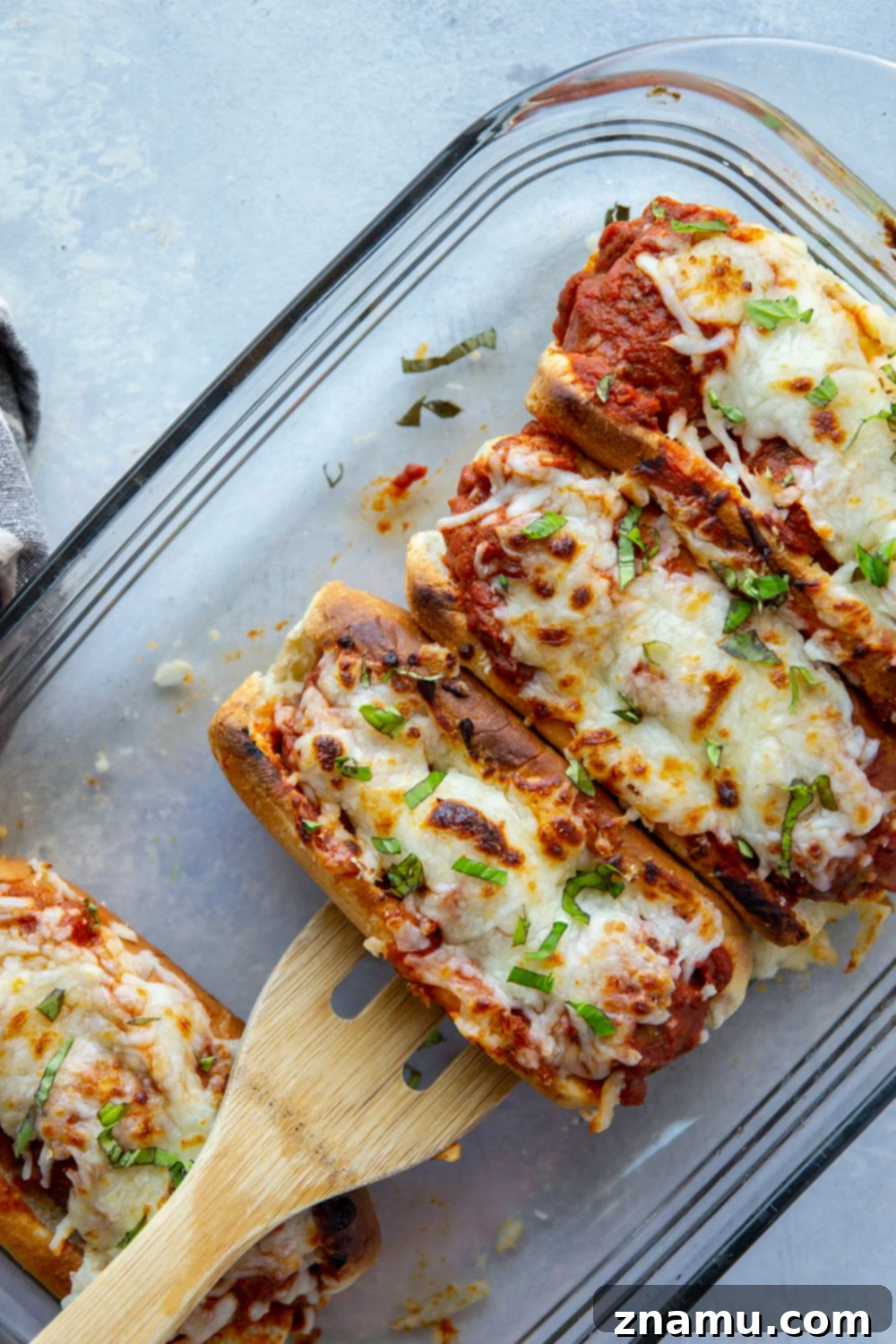 Cheesy Baked Meatball Subs 6 Overhead view of several baked meatball marinara subs in a baking dish, garnished with basil.