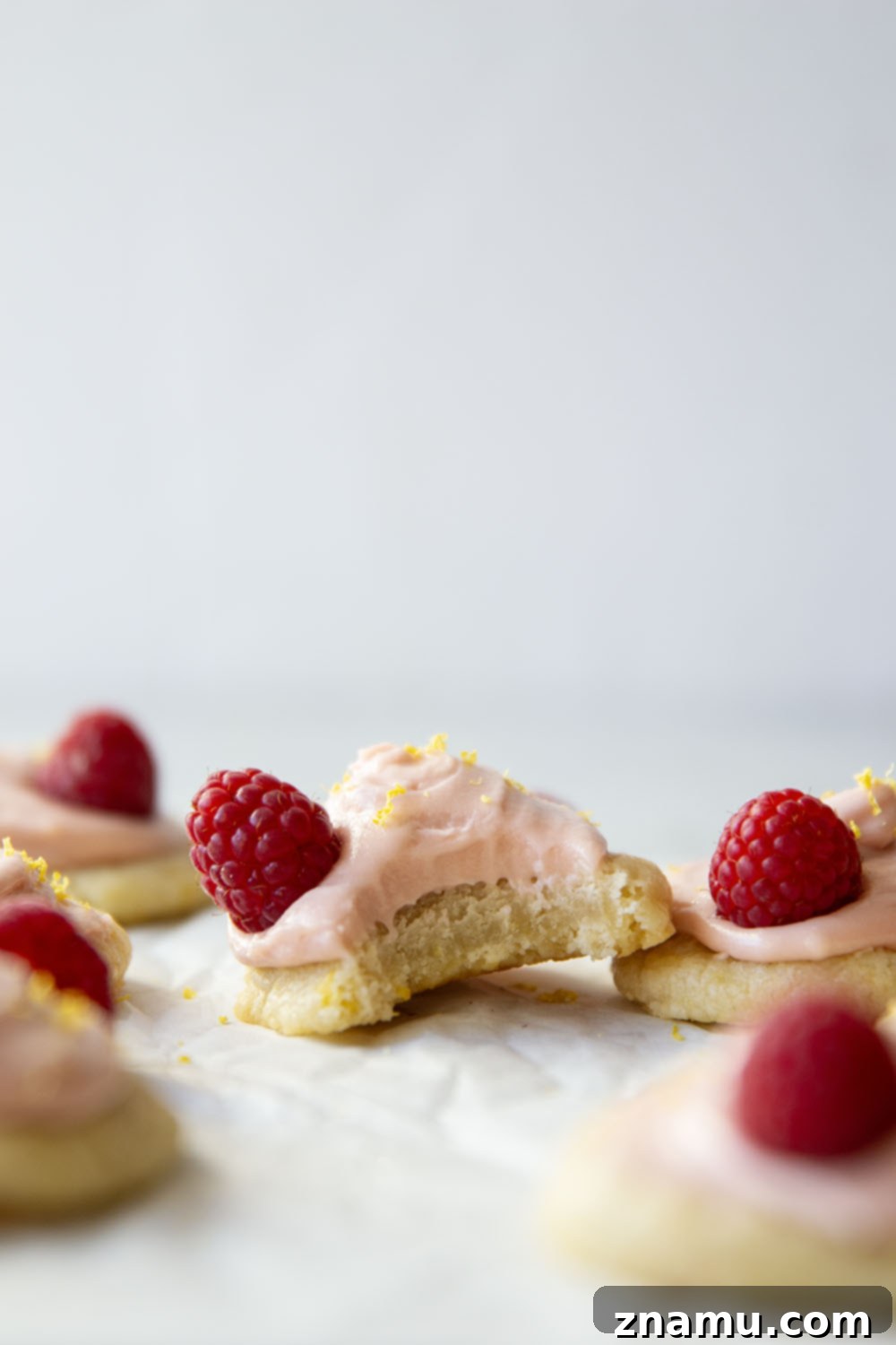 Close-up of a lemon shortbread cookie with pink raspberry cream cheese frosting and fresh raspberries