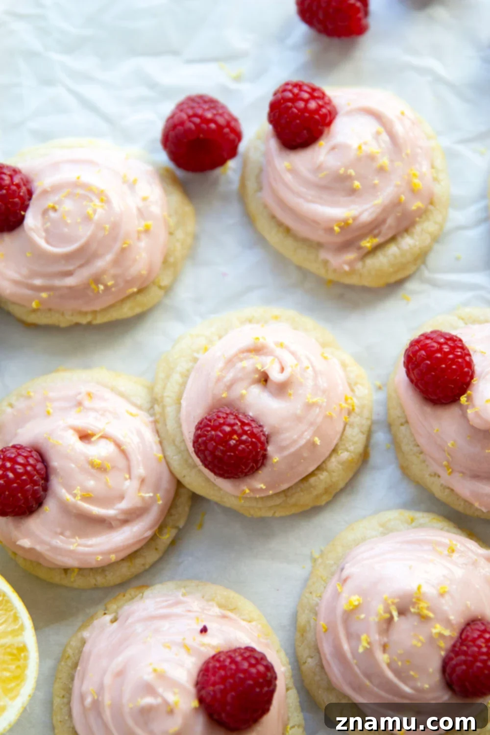 A stack of pink-frosted lemon shortbread cookies garnished with fresh raspberries and lemon zest