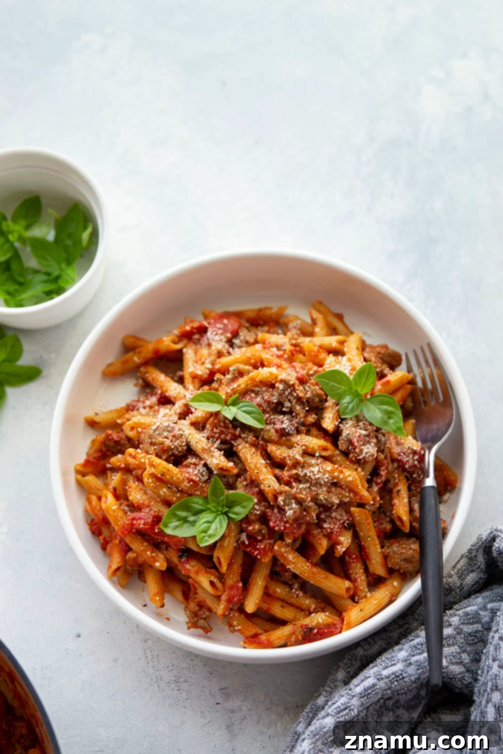 Smoky Red Pepper & Sausage Vodka Pasta 5 A close-up of the Penne alla Vodka with Sausage sauce simmering in a Dutch oven, with basil leaves and roasted red peppers visible, creating a rich texture.