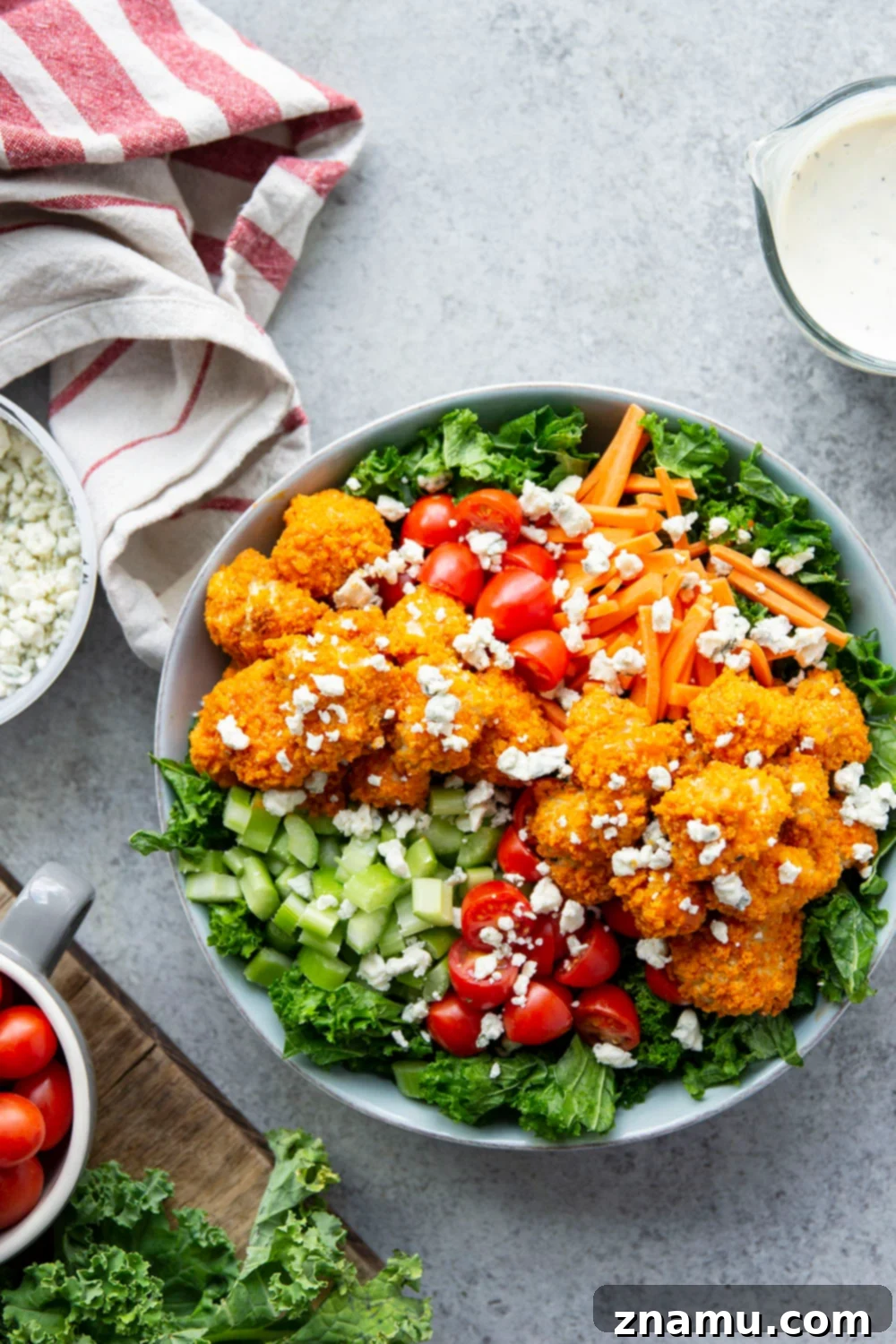 Fiery Buffalo Chicken Kale Delight 2 Crispy buffalo chicken nuggets, massaged kale, and fresh vegetables drizzled with creamy buttermilk ranch dressing and blue cheese in a large salad bowl.