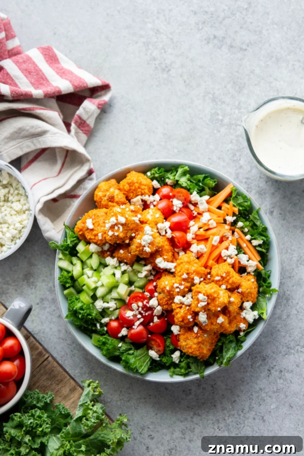 Fiery Buffalo Chicken Kale Delight 3 A close-up of a colorful buffalo chicken kale salad with visible crispy chicken, kale, tomatoes, celery, and blue cheese crumbles.