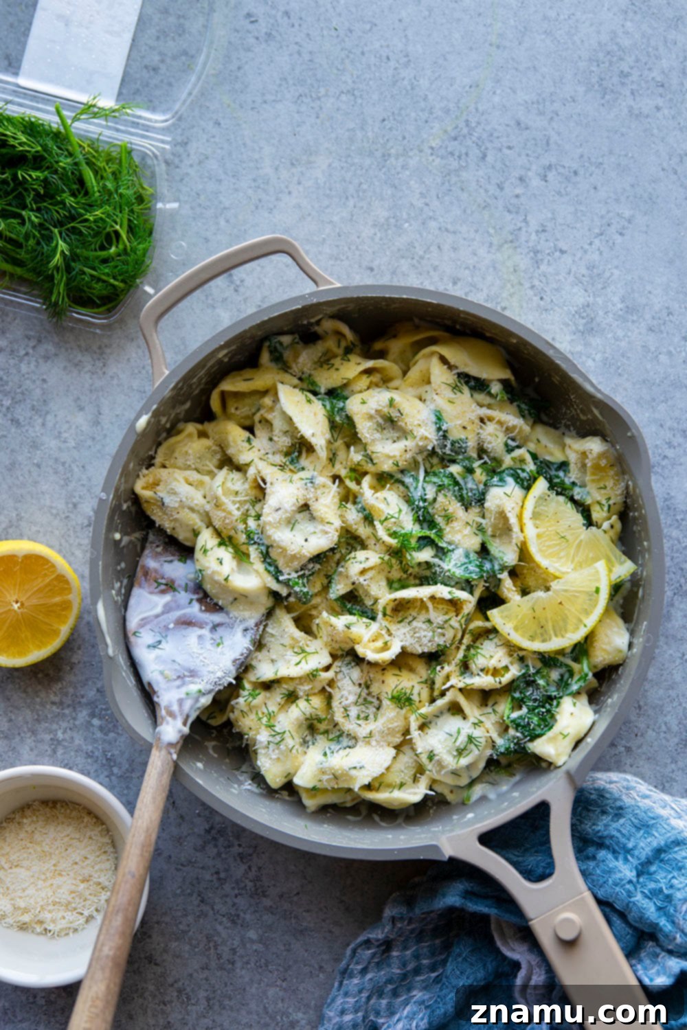 Zesty Lemon Dill Alfredo Tortellini 3 Close-up of spinach alfredo tortellini with a spoonful, showing the creamy sauce and wilted spinach.