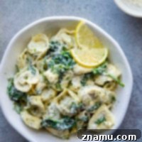 A small bowl of creamy lemon dill spinach alfredo tortellini, garnished with fresh dill.