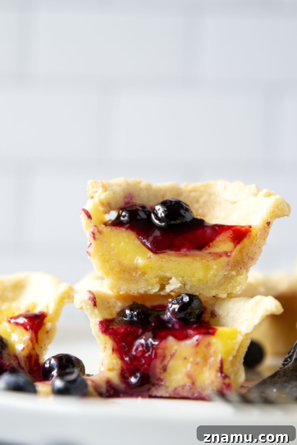 Sunshine Lemon & Blueberry Tartlets 6 An array of finished mini lemon tarts, beautifully arranged, some with spoons of blueberry sauce, others with hints of lemon zest.