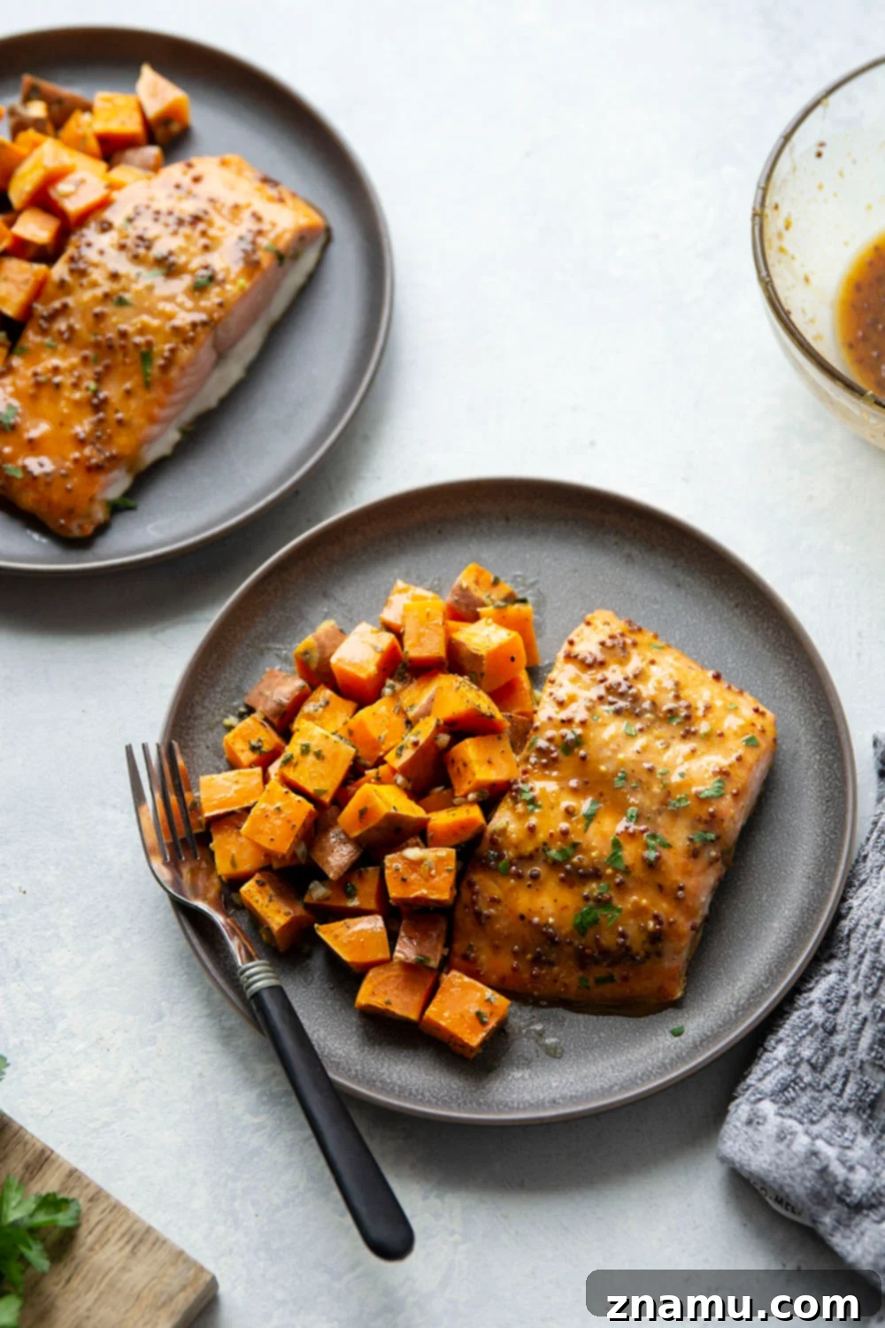 Honey Mustard Salmon with Garlic Butter Roasted Sweet Potatoes 5 A hand spoons honey mustard glaze over raw salmon fillets on a sheet pan with roasted sweet potatoes.
