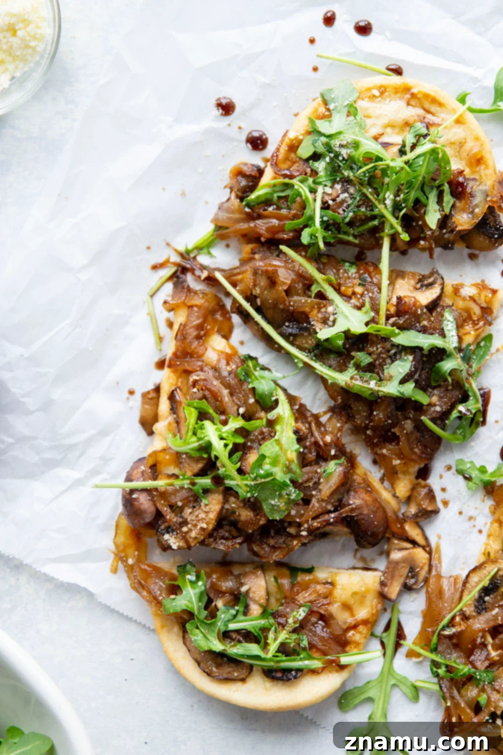 A vibrant Caramelized Onion Mushroom Flatbread featuring golden caramelized onions, sliced mushrooms, melted Parmesan and Gruyere cheeses, and a generous topping of fresh arugula with balsamic glaze.