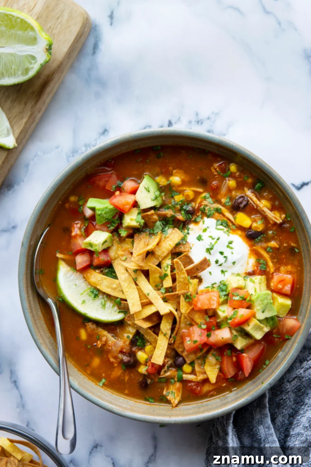 Easy Instant Pot Chicken Tortilla Soup 5 Various vibrant toppings for chicken tortilla soup, including avocado, cilantro, lime, and shredded cheese, arranged around a serving bowl.