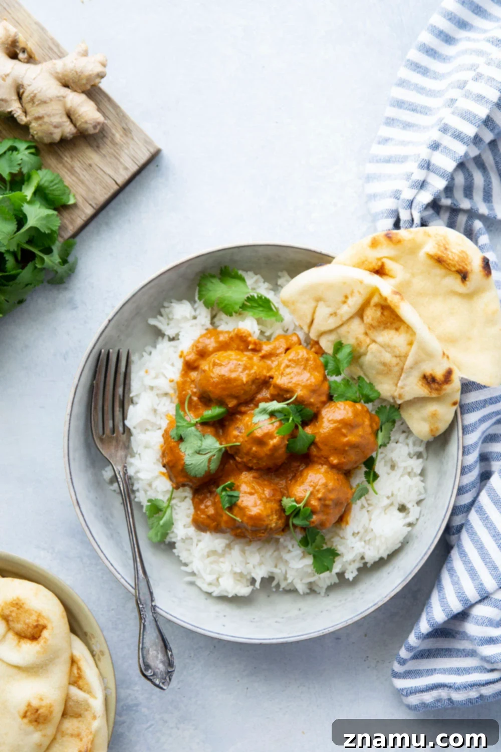 Creamy Instant Pot Butter Chicken Meatballs 6 An overhead shot of a full bowl of Instant Pot Butter Chicken Meatballs with rice, naan, and cilantro, ready for enjoyment.
