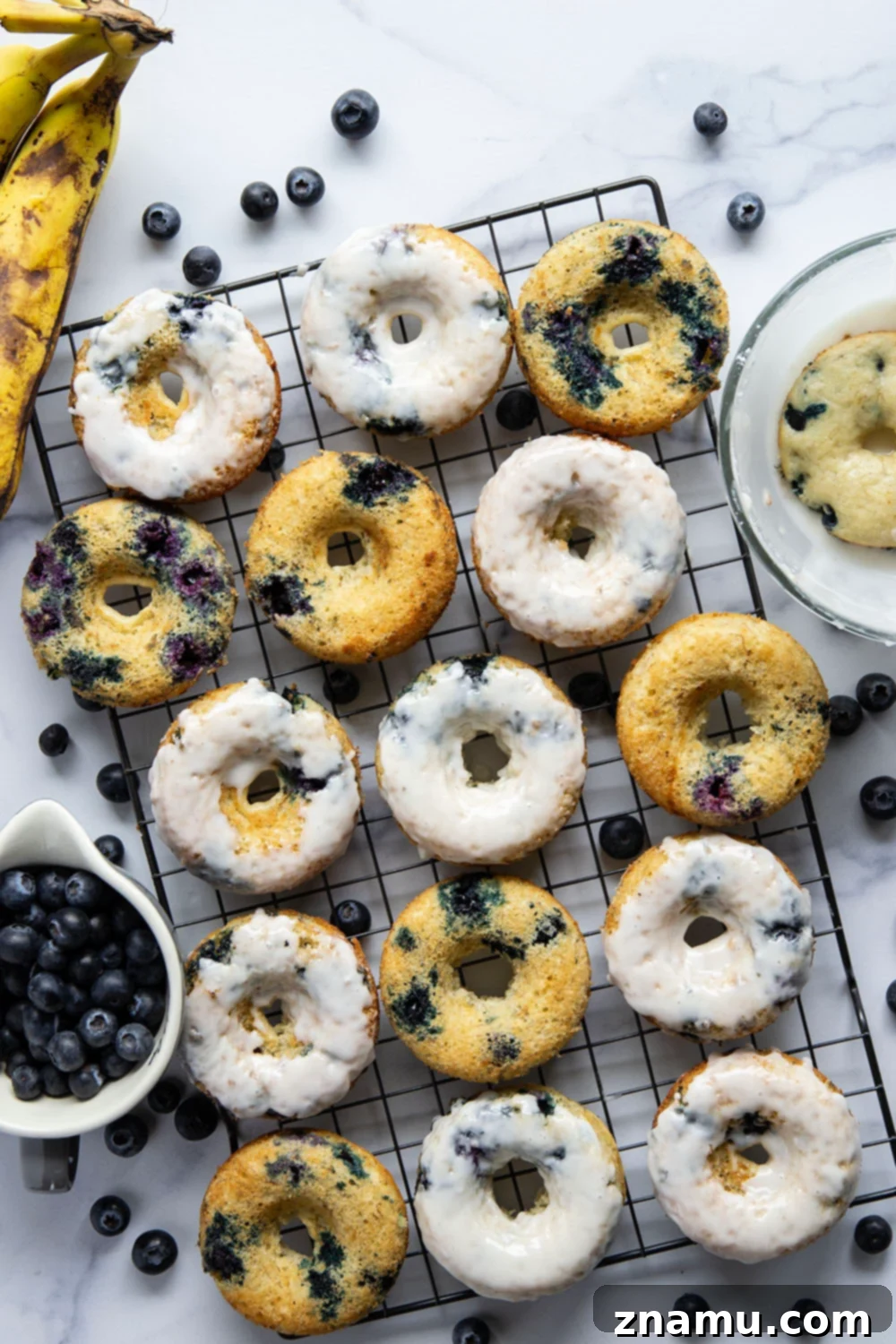 Blueberry Banana Vanilla Donuts 2 Close-up of a perfectly baked blueberry banana donut, showing its incredibly moist interior, studded with vibrant juicy blueberries, and generously dipped in creamy vanilla glaze.