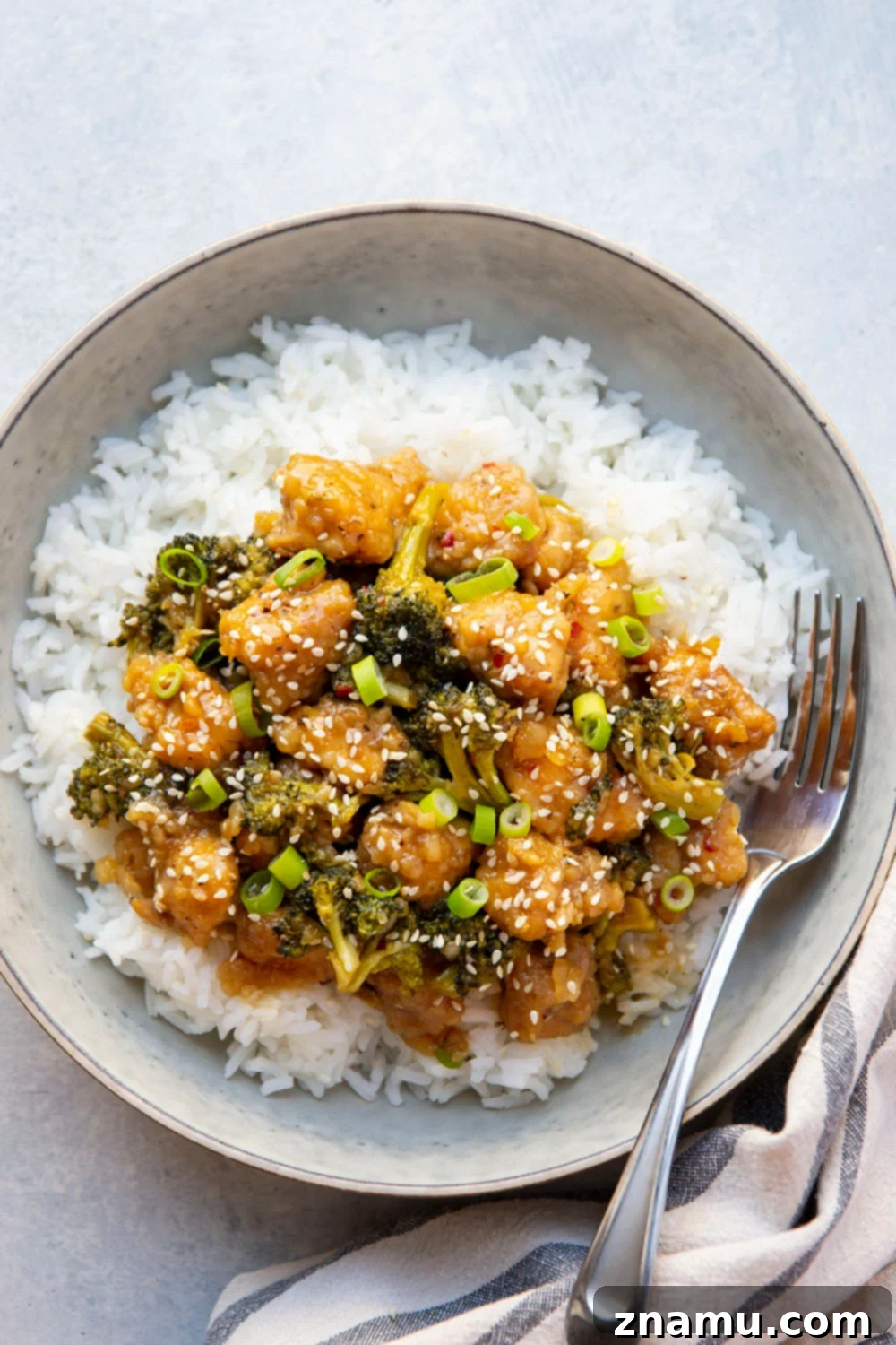 Sticky Honey Bourbon Chicken and Broccoli 5 A hand stirring Honey Bourbon Chicken and Broccoli in a large skillet, showing the glossy sauce coating the ingredients.